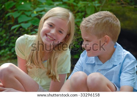 brother with older sister sitting down outdoors talking to each other and smiling