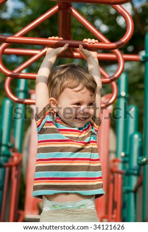 little two year old boy playing on bars at a playground