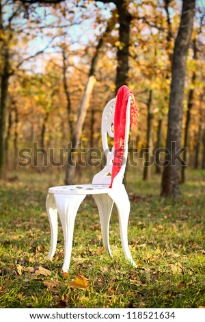 White chair in the autumn forest on a chair hanging pink scarf