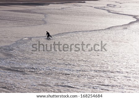 Putsborough Sands, UK -  December 11, 2013: A lone surfer leaves the water and makes his way up the beach in the late afternoon. This stretch of coastline has long been popular with surfers in England