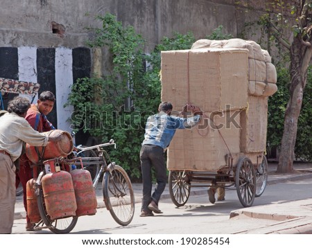 DELHI, INDIA - MARCH 28, 2014: Heavy loads being towed by porters through the heart of the old city. The use of porters to transport goods consignments in this way is common in Indian towns and cities