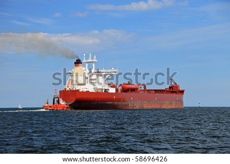 Red tug introduces the tanker into sea.