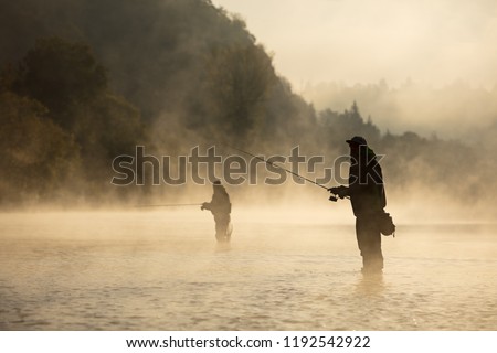 Men fishing in river with fly rod during summer morning. Beautiful fog.