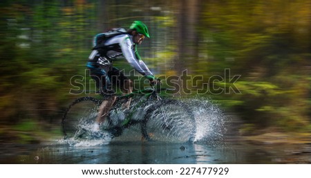Mountain biker speeding through forest stream. Water splash in freeze motion.