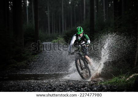 Mountain biker speeding through forest stream. Water splash in freeze motion.