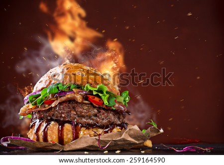 Delicious hamburger with fire flames on wooden background