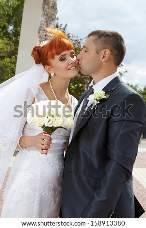 Young couple on a formal wedding photo  The groom kisses his bride while her eyes are closed