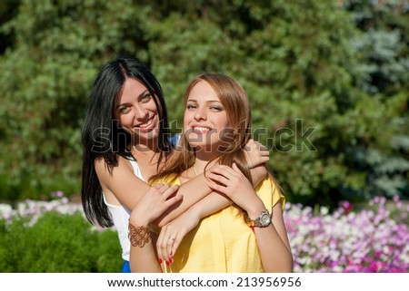 Beauties in style. Two beautiful young well-dressed women smiling at camera while standing embracing outdoors