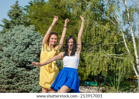 Beauties in style. Two beautiful young well-dressed women smiling at camera while standing with arms raised funny outdoors