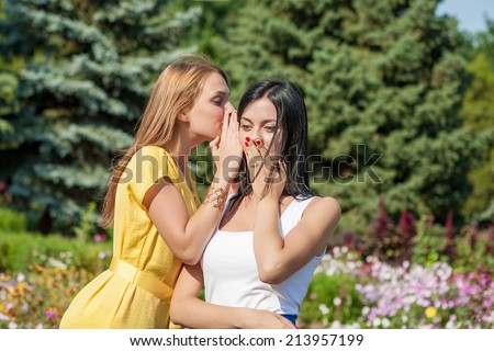 Friendly talk. Two beautiful young women walking near the flowerbed and talking