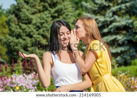 Friendly talk. Two beautiful young women walking near the flowerbed and talking