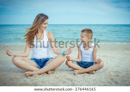 Happy family. Young happy beautiful  mother and her son doing yoga on coast of sea on beach