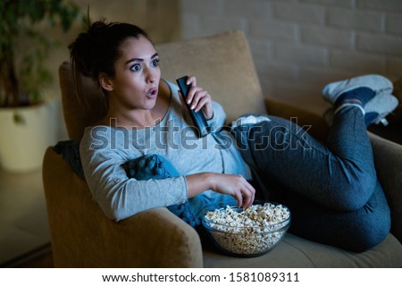 Young woman in disbelief watching TV while eating popcorn in the evening at home.  Stock fotó © 
