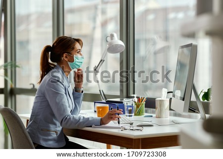 Young businesswoman wearing face mask while working on a computer in the office. 