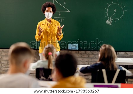 Black teacher with protective face mask teaching her students on a class at elementary school.