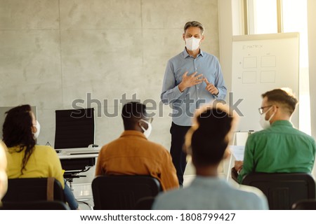 University professor wearing protective face mask while holding a class to group of students during coronavirus epidemic. 