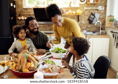 Happy African American woman having Thanksgiving lunch with her family and serving salad at dining table.  ストックフォト © 