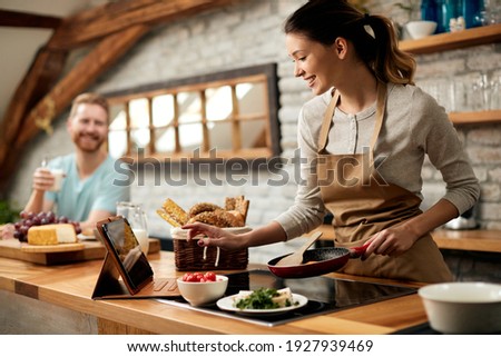 Happy woman preparing food while following recipe on digital tablet in the kitchen. 
