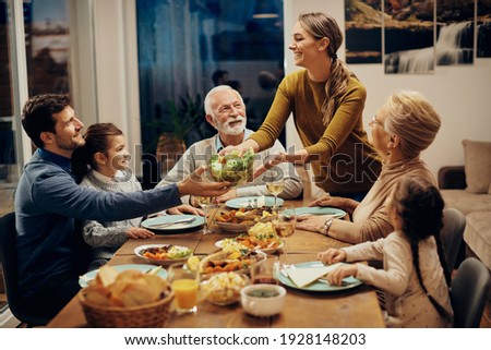 Happy multi-generation family enjoying in a lunch together at home. Focus is on young woman serving salad at dining table. 
