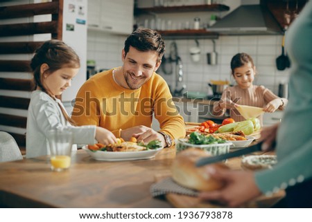Happy family preparing dining table for lunch at home. Focus is on father. 