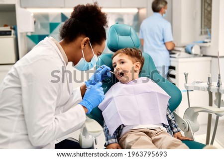 Black female dentist examining small boy's teeth during dental procedure at dentist's office. Focus is on boy. Stockfoto © 