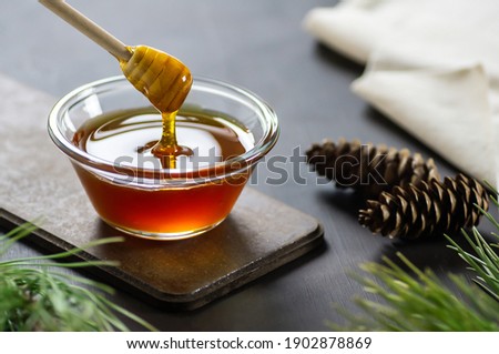 Pine honey in jar or bowl with honey stick and pine cones on rustic table, healthy food 