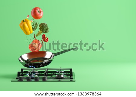 Fresh colored vegetables flying from the stainless steel frying pan. At the bottom - a cooking stove with burning fire. Green studio background