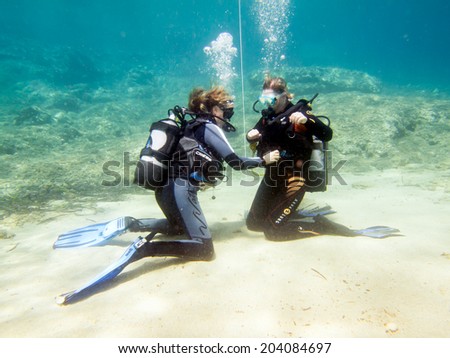 HALKIDIKI,GREECE-JULY 09 2014 : Two female scuba divers practise their skills underwater before a dive.Scuba diving is a sport carried out in many places around the world
