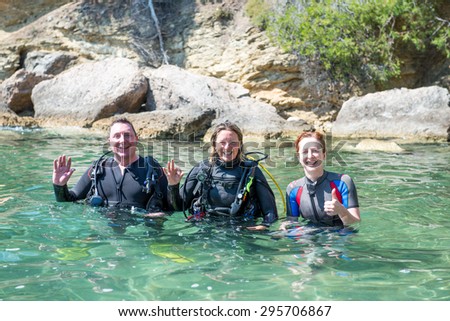 Three Scuba Divers standing in shallow water before a dive.Two of them are wearing their scuba equipment.