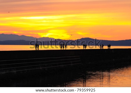 sunset scene of people walking on Ogden point breakwater in twilight, victoria, british columbia, canada