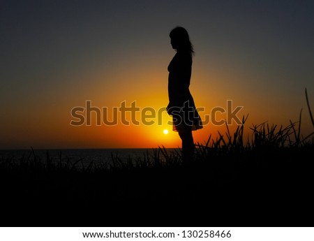 Profile of woman sitting on the grass near the sea at sunset