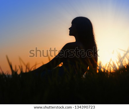 Profile of woman sitting on the grass near the sea at sunset