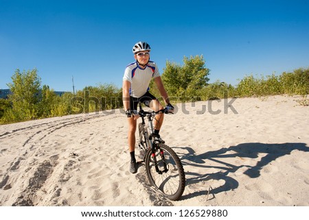 A male cyclist riding a bike stopped rolling on the sand; clear summer day