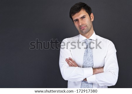 Young handsome man in black suit smiling on white background with crossed arms