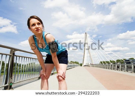 young woman resting after run. in blue sportswear. over the bridge