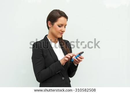 Business woman dialing and standing against the glass wall in the city.