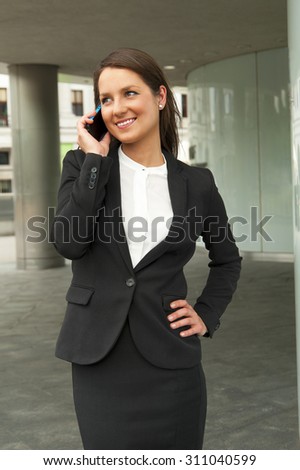 Business woman talking by smart phone against the glass wall in the city.