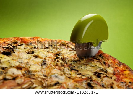 Italian pizza with cheese, mushrooms and ham on a green background and with green pizza cutter