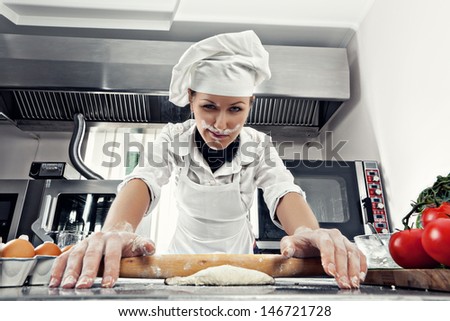 Professional female chef rolls out the dough for making bread in a professional kitchen. Flour dust on the face