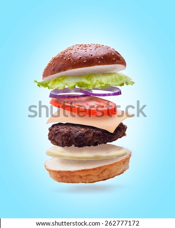 delicious burger with flying ingredients on light blue background