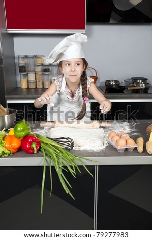 little girl chef kneads the dough with a rolling pin on the kitchen table with raw food