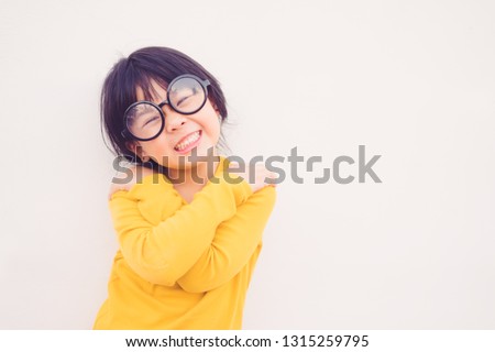Happy smiling smart and nerd little asian girl in glasses.Portrait confident smiling little girl holding hugging herself isolated white wall background.Positive human emotion, attitude, Love yourself. 商業照片 © 