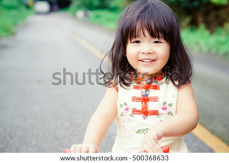 Happy Little Asian Girl On A Bicycle Caught In Motion On A Driveway Happy Little Asian Girl On A Bicycle Caught In Motion On A Driveway