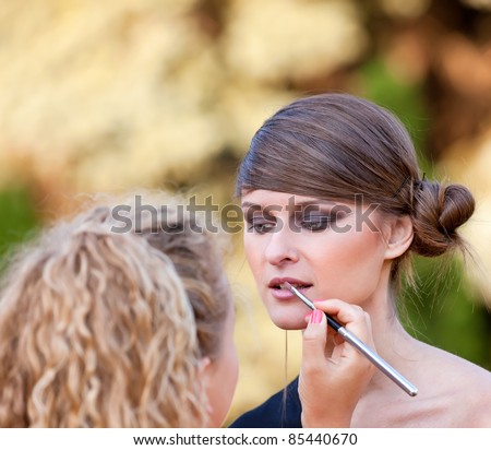 Makeup master applying lipstick with brush on caucasian girl lips