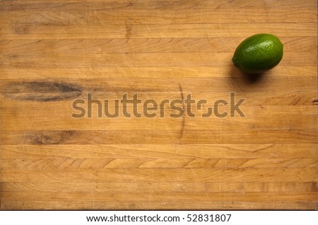A lime sits on a worn butcher block cutting board