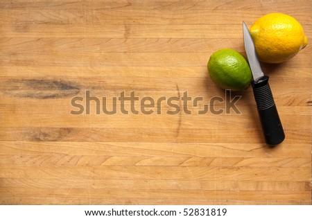 A lime and a lemon sit waiting to be cut with a knife on a worn butcher block cutting board