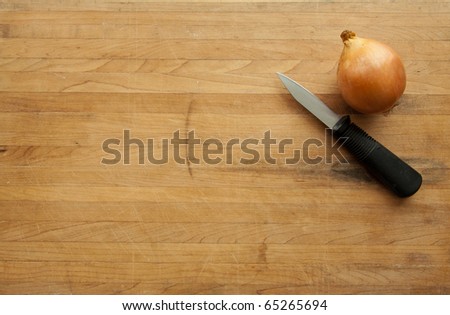 An onion and a knife sit on a worn butcher block cutting board with sufficient room for text