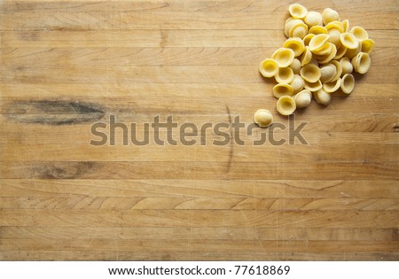 A group of uncooked orecchiette sits in the corner of a worn cutting board