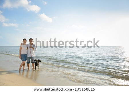 Asian couples with dog at beach against sunlight