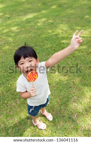 Little girl eat lollipop with smiling face and hand up
